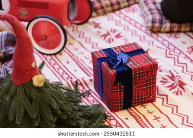 A beautifully wrapped gift box in plaid paper with a navy ribbon, placed on a festive patterned blanket alongside a whimsical gnome and a vintage toy car. - Powered by Shutterstock