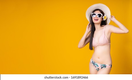 Beautiful,Sexy asian girl standing on yellow background in a pink bikini and smiling.Summer vocation happy trip concept.