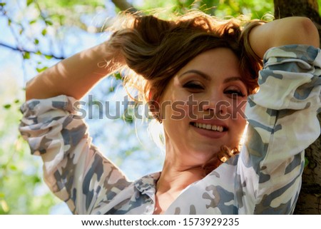 Beautirul girl with curly blonde hair near a tree in the park with sunny weather in a summer, spring or autumn day