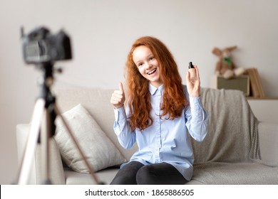 Beauty Advice And Blog. Smiling female teen doing makeup, recording cosmetics product review, showing her foundation for young skin to camera on tripod. Girl filming video, showing thumbs up