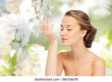 beauty, aroma, people and body care concept - young woman smelling perfume from wrist of her hand over green natural background with cherry blossoms