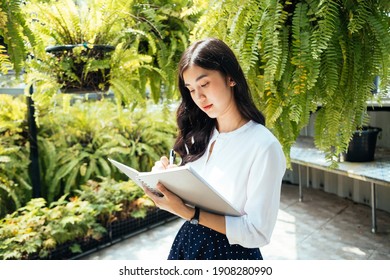 Beauty Asian Woman Writing On A Notebook In The Tropical Garden.