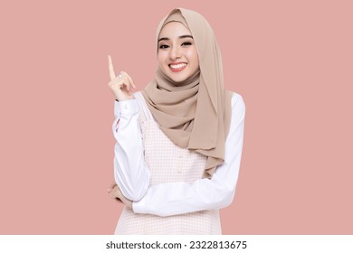 Beauty Asian young muslim girl wear hijab headscarf smiling and pointing finger to copy space isolated on pink background. - Powered by Shutterstock