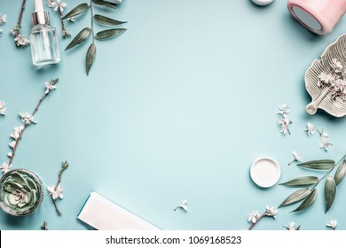 Schöner Hintergrund mit Kosmetikprodukten für Gesichter, Blättern und Kirschblüten auf pastellblauem Hintergrund. Modernes Federhaut-Design, Draufsicht, flache Lage. 
