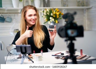 Beauty blogger woman filming daily make-up routine tutorial near camera. Influencer girl live streaming cosmetics product review. Vlogger female recommends eye shadow palette showing thump up sign.