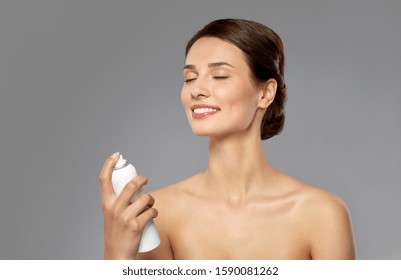 Beauty, Bodycare And People Concept - Beautiful Young Woman Applying Facial Spray Or Mist To Her Face Skin Over Grey Background