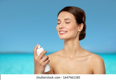 Beauty, Bodycare And People Concept - Beautiful Young Woman Applying Facial Spray Or Mist To Her Face Skin Over Blue Sea And Sky Background