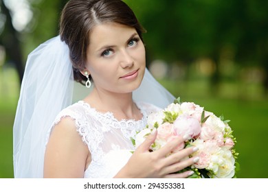 Beauty bride in bridal gown with bouquet and lace veil on the nature. Beautiful model girl in a white wedding dress. Female portrait in the park. Woman with hairstyle. Cute lady outdoors