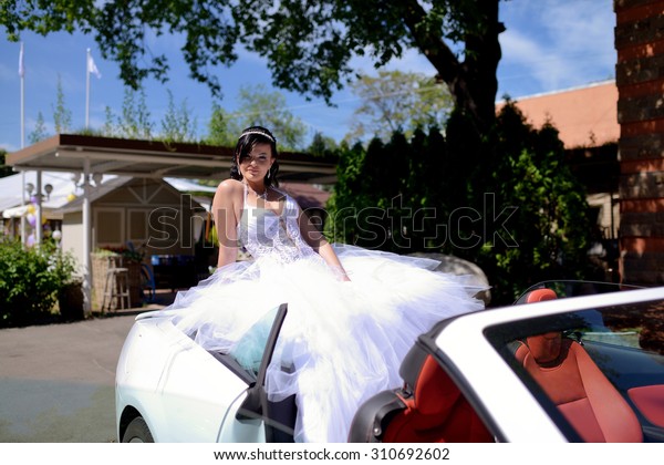 Beauty bride in bridal gown in the\
car. Beautiful model girl in a white wedding dress. Female portrait\
in the auto. Woman with hairstyle. Cute lady\
outdoors