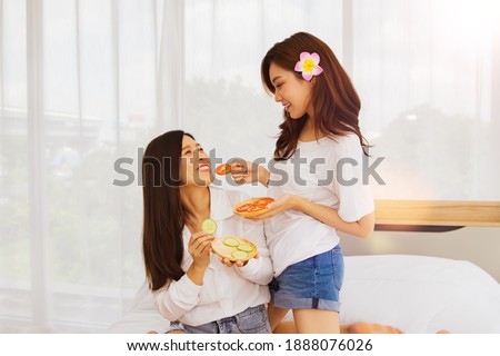 Beauty can be done easily at home : Portrait Two beautiful young asian teases wanting to eat cucumber and shredded tomato lying relax in the house with fun, they use natural products for facial care.