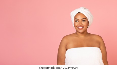 Beauty Care. Attractive Oversized African American Lady Wrapped In Towel Posing Standing Over Pink Studio Background, Smiling Looking Aside. Female Selfcare And Pampering. Panorama With Empty Space