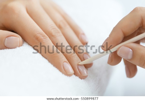 Beauty Care. Closeup Beautiful Woman Hand With\
Healthy Natural Nails Receiving Cuticle Removing Procedure With\
Wooden Cuticle Pusher Remover Stick In Salon. Manicure On Female\
Hands. High Resolution