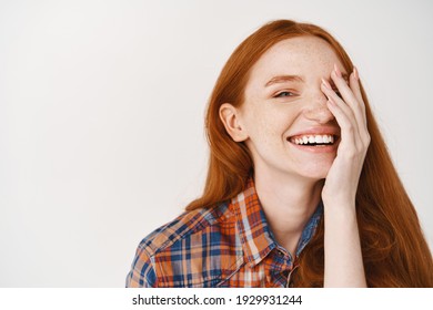 Beauty. Close-up Of Happy Young Woman With Red Natural Hair And Pale Skin, Smiling Joyfully And Covering Half Of Face, Standing Over White Background