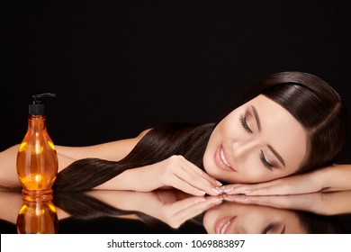 Beauty Concept, Brunette Woman With Closed Eyes Lying On Black Glass With Her Reflexion. Gorgeous Model With Hair Oil Near Her, Head And Shoulders, Beauty Portrait