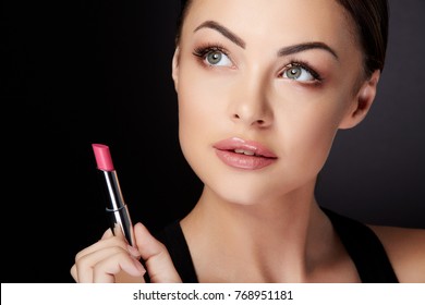 Beauty Concept, Head And Shoulders Of Woman Looking Up And Aside, Holding Rose Lipstick. Beauty Portrait Of Model With Rose Lips Painted With Lip Gloss, Studio With Black Background