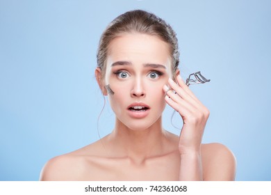 Beauty Concept, Head And Shoulders Of Young Woman With Natural Makeup. Shocked Girl Holding Instrument For Curling Lashes And Looking At Camera, False Lashes. Studio, Indoors 