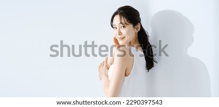 beauty concept image of an attractive asian woman with ultra violet protection and sunscreen,
wearing white sleeveless dress,
in white room with sunlight.