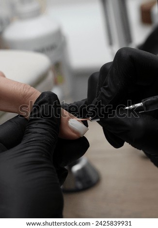 Beauty concept. A manicurist in black latex gloves makes a hygienic manicure and paints the client's nails with gel polish in a beauty salon. Close-up. Vertical.