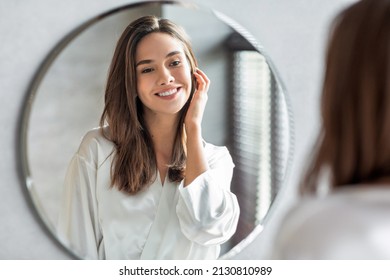 Beauty Concept. Portrait Of Attractive Happy Woman Looking At Mirror In Bathroom, Beautiful Millennial Lady Wearing White Silk Robe Smiling To Reflection, Enjoying Her Appearance, Selective Focus - Shutterstock ID 2130810989