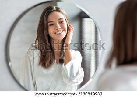 Beauty Concept. Portrait Of Attractive Happy Woman Looking At Mirror In Bathroom, Beautiful Millennial Lady Wearing White Silk Robe Smiling To Reflection, Enjoying Her Appearance, Selective Focus