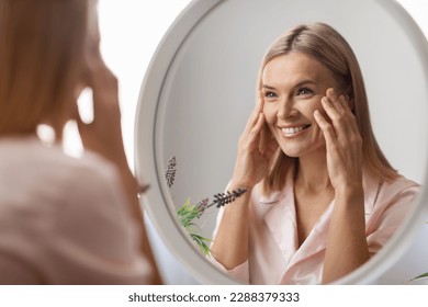 Beauty Concept. Portrait Of Attractive Mature Woman Looking At Mirror In Bathroom, Beautiful Middle Aged Lady Touching Her Flawless Face Skin And Smiling To Reflection, Selective Focus - Shutterstock ID 2288379333
