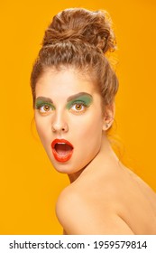 Beauty concept. Portrait of surprised pretty woman with colorful makeup on a yellow  background. Makeup and cosmetics. Studio shot. 