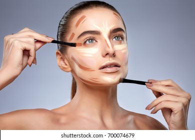 Beauty concept. Portrait of woman with contouring on face, doing make-up. Types of drawing make-up, woman with nude make-up looking up, holding brushes for make-up