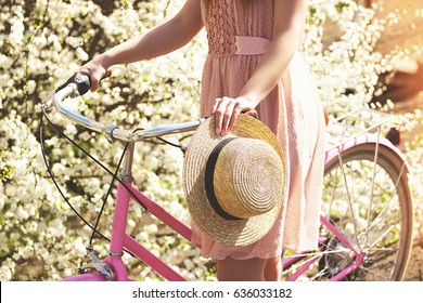 Beauty concept. Portrait of young and beautiful girl in pink dress standing with retro bike on flower background. Vintage bike concept.