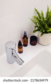 Beauty Cosmetic Product Bottle In Brown Glass And Green Potted Plant On A White Sink In Bathroom With Copy Space. Eco Friendly Sustainable Skin Care. Minimal Home Interior. Morning Beauty Routine.