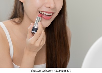 Beauty cosmetics concept, hand of asian young woman, girl make up face by applying lipstick, lips balm on her mouth, looking at the mirror at home. Female look with natural fashion style, skin care. - Powered by Shutterstock