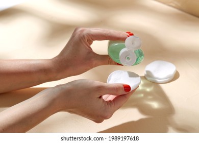 beauty, cosmetics and skincare concept - close up of hands applying lotion to cotton pad over beige background with shadows - Shutterstock ID 1989197618