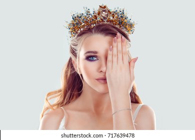 Beauty crowned queen girl woman miss bride hand on, covering face showing manicure gel art nails in set with lips color looking at you camera on white. Full makeup golden blue crystals crown pastel