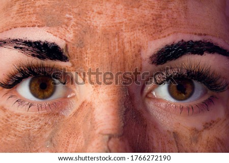 Beauty day. Close-up of a woman`s face. The woman has a clay face mask and eyebrows painted black.