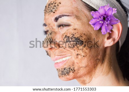 Beauty day. Close-up of a woman`s face. The woman has a clay face mask and eyebrows painted black.Woman`s face with a clay brown mask WITH 
 COFFEE GROUNDS and eyebrows painted black.