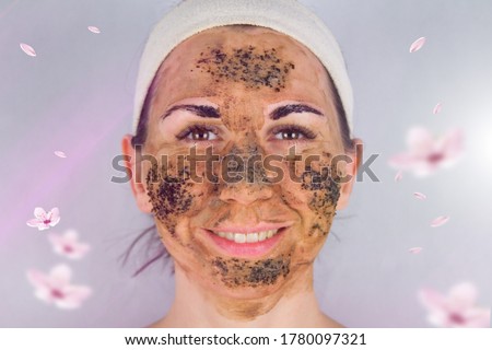 Beauty day. Close-up of a woman`s face. The woman has a clay face mask and eyebrows painted black.The woman stares into the lens.Woman`s face with a clay brown mask and eyebrows painted black.