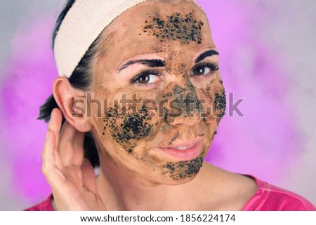 Beauty day. Close-up of a woman`s face. The woman has a clay face mask ,COFFEE PEELING and eyebrows painted black.