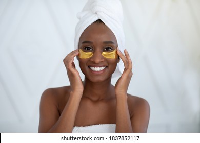 Beauty day and home skin care. Smiling young african american female with towel on head after shower applying golden patches under eyes to moisturize, in bedroom interior, white background, free space - Powered by Shutterstock