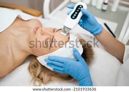 Beauty doctor with ultrasonic scraber doing procedure of ultrasonic cleaning of face. Cosmetology and facial skin care