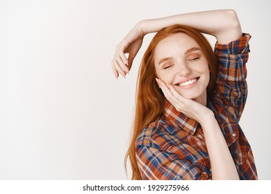 Beauty. Dreamy girl teenager with red natural hair, posing on white background, smiling happy with eyes closed, touching perfect face without makeup.