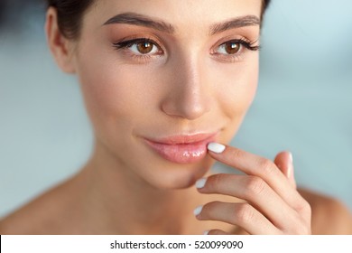 Beauty Face. Beautiful Woman With Natural Makeup And Sexy Full Lips Touching Her Mouth. Closeup Portrait Of Smiling Model Girl With Healthy Smooth Facial Skin Applying Lip Balm On Lip. High Resolution