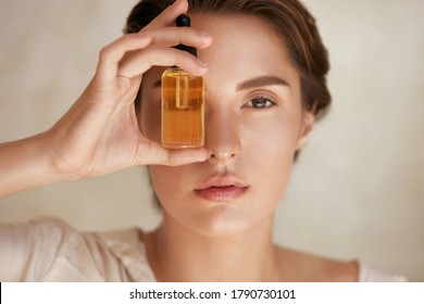 Beauty Face. Close Up Portrait Of Woman With Bottle Of Essential Oil. Beautiful Model With Radiant And Glowing Facial Skin Looking At Camera. Moisturizing With Serum Collagen And Hyaluronic Acid.