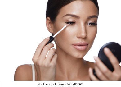 Beauty Face. Closeup Of Sexy Young Woman With Concealer Brush And Mirror In Hands. Portrait Of Beautiful Healthy Female Model Applying Concealer Under Eyes. Skin Cosmetics. High Resolution