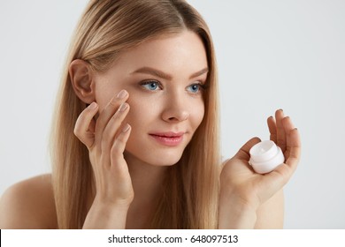 Beauty Face Cosmetics. Closeup Of Beautiful Female Model Putting Cream On Skin Under Eyes. Portrait Of Sexy Young Woman Holding Bottle Of Cosmetic Skin Care Product Bottle In Hand. High Resolution