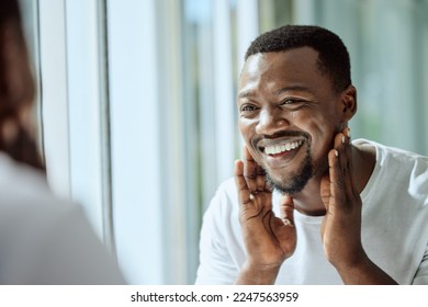 Beauty, face and skincare with a black man looking in the bathroom mirror during his morning routine at home. Skin, head and reflection with a handsome male grooming for wellness or natural care - Powered by Shutterstock