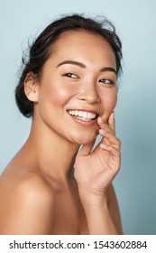  Schönes Gesicht. Lächelnde asiatische Frau, die gesundes Hautporträt berührt. Schönes, fröhliches Mädchenmodell mit frisch glühender, hydrierter Gesichtshaut und natürlichem Make-up auf blauem Hintergrund im Studio. Hautpflegekonzept
