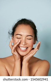Beauty face. Smiling asian woman touching healthy skin portrait. Beautiful happy girl model with fresh glowing hydrated facial skin and natural makeup on blue background at studio. Skin care concept - Shutterstock ID 1543602941