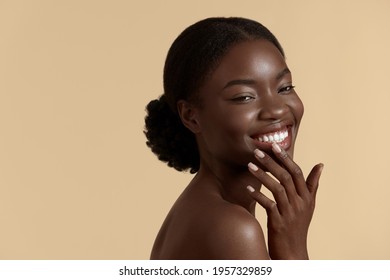 Beauty Face. Smiling Black Woman Touching Healthy Skin Portrait. Beautiful Girl With Fresh Glowing Hydrated Facial Skin And Natural Makeup On Blue Background At Studio. Skin Care Concept