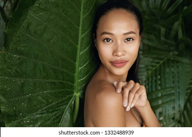 Beauty Face. Woman Model With Natural Makeup And Healthy Skin In Tropical Nature. Beautiful Asian Girl Portrait With Jungle Leaves On Background