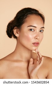 Beauty Face. Woman With Natural Makeup And Healthy Skin Portrait. Beautiful Asian Girl Model Touching Fresh Glowing Hydrated Facial Skin On Beige Background Closeup. Skin Care Concept