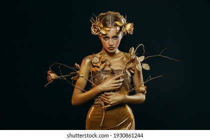 Beauty Fantasy Woman, Face In Gold Paint. Golden Shiny Skin. Fashion Model Girl, Image Goddess. Glamorous Crown, Wreath Roses, Jewellery Accessories. Professional Metallic Makeup. Hand Holds A Branch